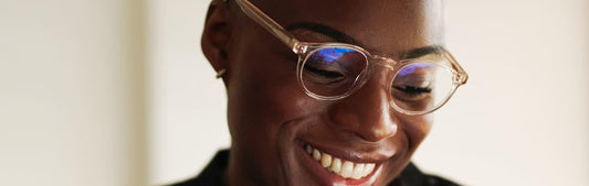 Femme souriante portant des lunettes rondes transparentes roses contre la lumière bleu 