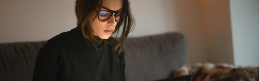 Femme portant des lunettes avec filtre anti-lumière bleue, en train d’acheter ses lunettes sur internet depuis son canapé